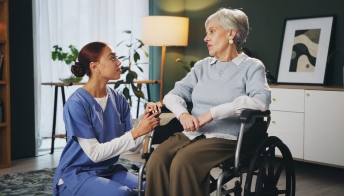Women, nurse and senior patient in wheelchair at retirement home for healthcare, support and checkup. Caregiver, person with a disability and conversation for medical service,  physiotherapy and care.