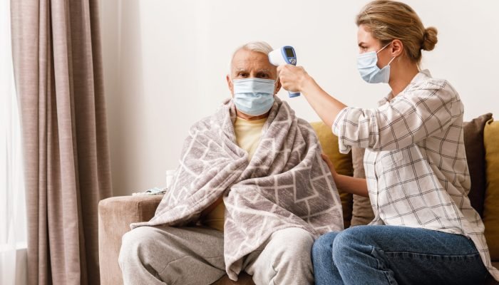 Young woman taking care of her elderly grandfather with a cold syptoms at home